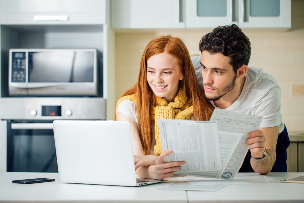Couple holding papers and looking at laptop screen